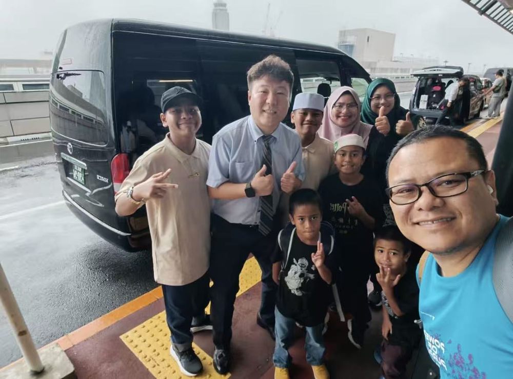 Driver welcoming a family beside a black Toyota Hiace at the airport